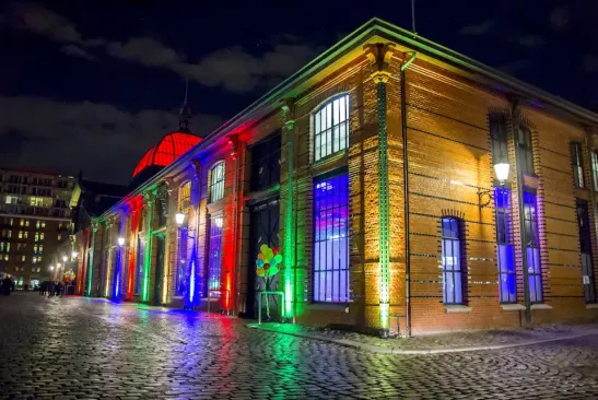 Fischauktionshalle die Wasserseite bei Nacht, festlich bunt beleuchtet mit bunten Luftballons und Kopfsteinpflaster im Vordergrund